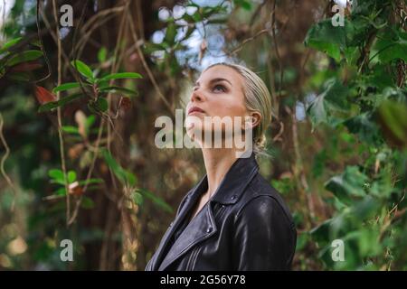 Moda in luoghi insoliti, giovane donna in giacca Edgy Moto nella foresta Foto Stock