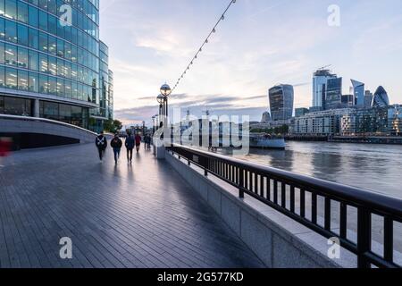 Persone che camminano per altri edifici londinesi sul lungofiume, moderni edifici per uffici con 20 Fenchurch Street o la torre Walkie-Talkie sullo sfondo al twilig Foto Stock
