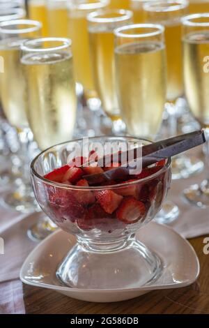 Fragole fresche in un recipiente di vetro con bicchieri di champagne sfocati sullo sfondo. Foto Stock