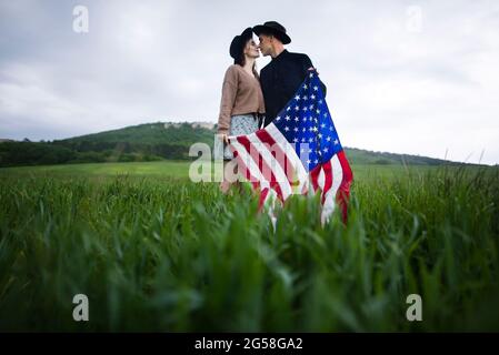 Giovane coppia con bandiera americana baciando in campo di grano Foto Stock