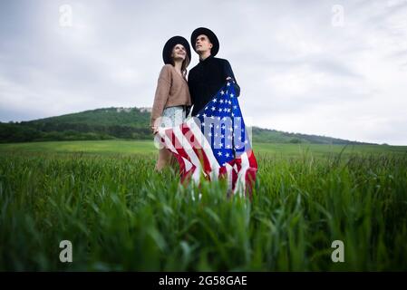 Giovane coppia che tiene bandiera americana in campo di grano Foto Stock