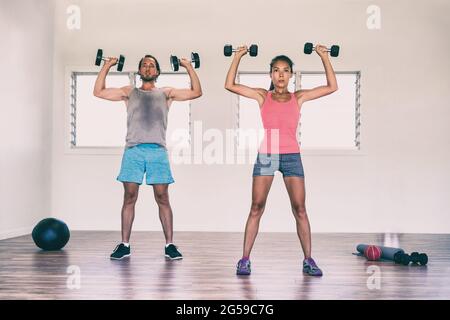 Fitness fit persone che allenano le braccia in palestra facendo pressione a spalla con pesi manubri o in piedi dumbbell pressa esercizio. Donna asiatica e. Foto Stock