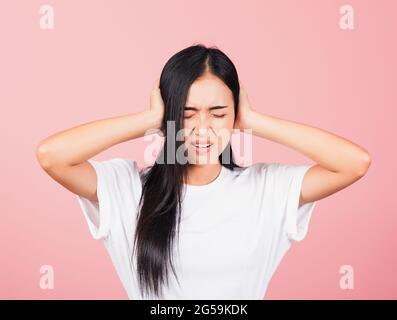 Ritratto asiatico bella giovane donna carina hanno orecchie chiuse con palme a mano e occhi stretti, studio girato isolato su sfondo rosa, thailandese femminile coperture Foto Stock