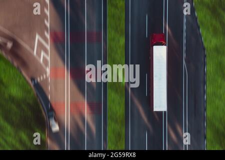 Un camion con cabina rossa e un rimorchio bianco guida in autostrada, per la consegna di merci - Drone Motion Blur Shot sospeso. Il modello di concetto di logistica e trasporto delle merci. Carrello su strada. Foto Stock