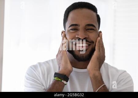 Felice razza mista uomo africano che tocca le morbide stoppie, barba elegante Foto Stock