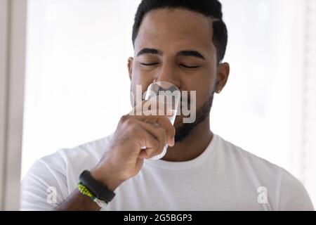 Positivo ragazzo nero rilassato godendo di acqua fresca pura fredda a casa Foto Stock