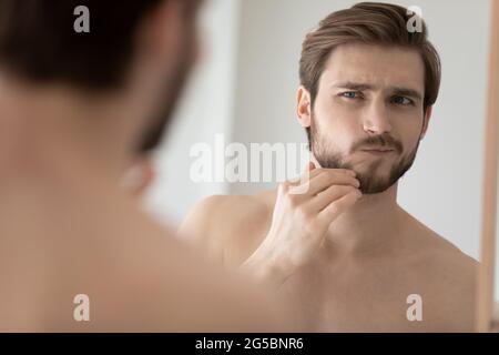Preoccupatevi giovane bell'uomo che esamina il volto in riflessione speculare Foto Stock