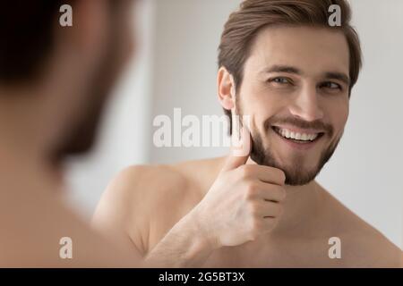 Felice millenario giovane bell'uomo che guarda nello specchio in bagno Foto Stock