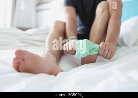 L'uomo mette la calza turchese sulla gamba mentre si siede sul letto Foto Stock