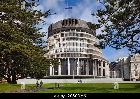 L'edificio del Parlamento Beehive incorniciato da alberi e prato davanti a persone che camminano, Wellington, South Island, Nuova Zelanda Foto Stock