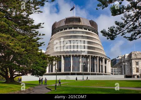 L'edificio del Parlamento Beehive incorniciato da alberi e prato davanti a persone che camminano, Wellington, South Island, Nuova Zelanda Foto Stock