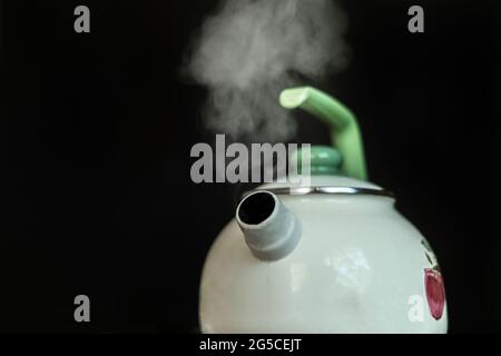 il bollitore con acqua bollente calda e il vapore fuoriesce su fondo scuro Foto Stock