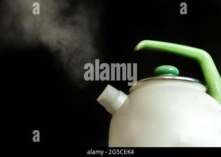 il bollitore con acqua bollente calda e il vapore fuoriesce su fondo scuro Foto Stock
