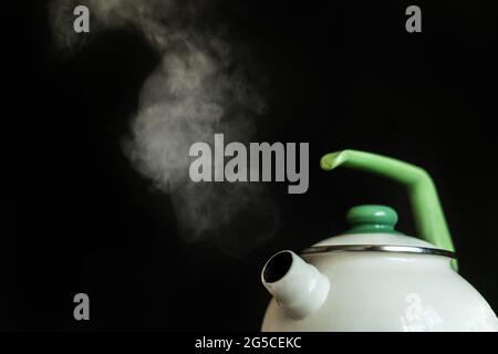 il bollitore con acqua bollente calda e il vapore fuoriesce su fondo scuro Foto Stock