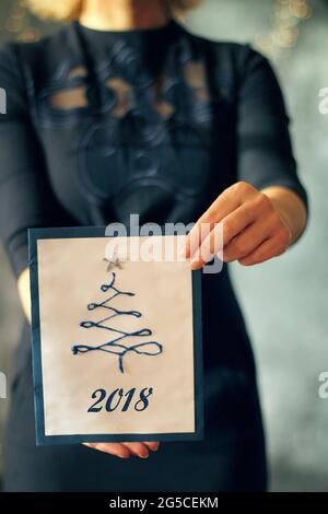 Ragazza che tiene una carta dell'albero di natale davanti a lei, faccia coperta, fuoco selezionato sulla carta e le mani, concetto di Natale Foto Stock