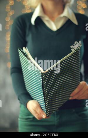 Ragazza che tiene un libro davanti a lei, faccia coperta, fuoco selezionato sulla carta e le mani, concetto di Natale Foto Stock