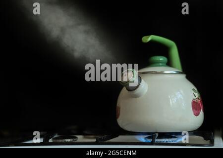 il bollitore con acqua bollente calda e il vapore fuoriesce su fondo scuro Foto Stock