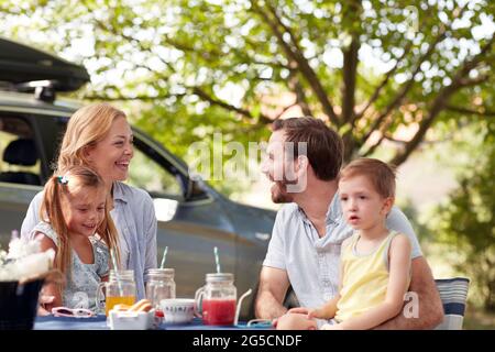 allegri genitori caucasici che si guardano a vicenda, sorridenti, ridenti, con i loro figli in giri Foto Stock