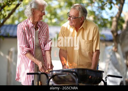 coppie caucasiche anziane che si guardano e sorridono, mentre fanno fuoco per barbecue Foto Stock