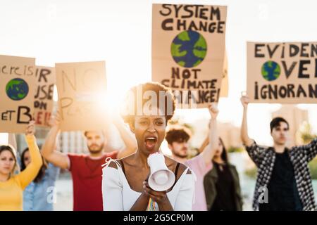 I manifestanti protestano contro l'inquinamento plastico e il cambiamento climatico - persone multirazziali che lottano su strada con bandiere Foto Stock