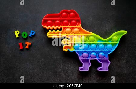 Giocattolo pop esso dinosauro arcobaleno colori su uno sfondo nero con lettere multicolore e lettere - Pop it. Foto Stock