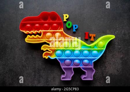 Giocattolo pop esso dinosauro arcobaleno colori su uno sfondo nero con lettere multicolore e l'iscrizione-Pop it sul retro. Foto Stock