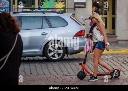 RIGA, LETTONIA. 30 agosto 2019. Foto con messa a fuoco selettiva. Donna con scooter elettrico cammina per strada. Foto Stock