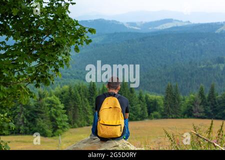 Solo ragazzo seduto sulla scogliera e godere di un tranquillo paesaggio verde montagne. Tranquillità e relax. Foto Stock