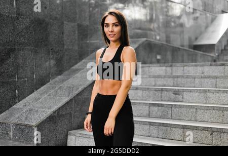 Ritratto di giovane donna sportiva conciata sullo sfondo di scale in marmo grigio all'aperto Foto Stock