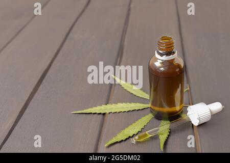 Olio CBD in una bottiglia di vetro con foglia verde di marijuana su sfondo di legno con spazio per la copia Foto Stock