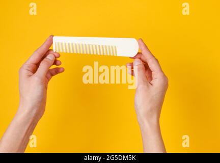 Le mani femminili tengono il pettine bianco di plastica su sfondo giallo. Cura dei capelli, concetto di bellezza. Vista dall'alto Foto Stock