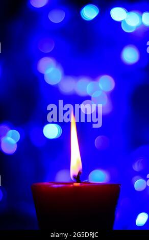 Luci a candela nel buio con colorati effetti di luce e bokeh per momenti solenni e carta da parati. Candela fiamma luce di notte con sfondo. Foto Stock