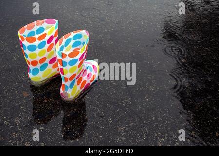 Colorati stivali a pois in pozza pioggia con gocce di pioggia Foto Stock