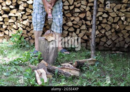 Uomo tritare legno con un'ascia nel cortile e un grande mucchio di ceppi tagliati sullo sfondo. Primo piano e spazio per la copia Foto Stock