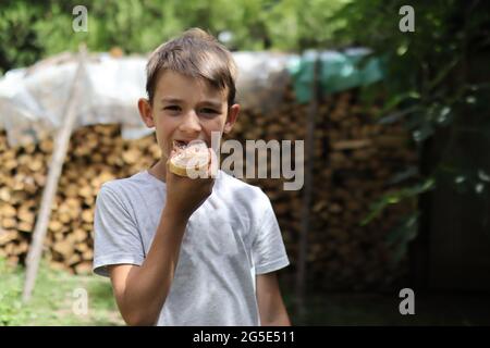 Un ragazzo mangia un pezzo di pane cosparso di cioccolato nella natura di una giornata estiva di sole. Primo piano e spazio per la copia Foto Stock