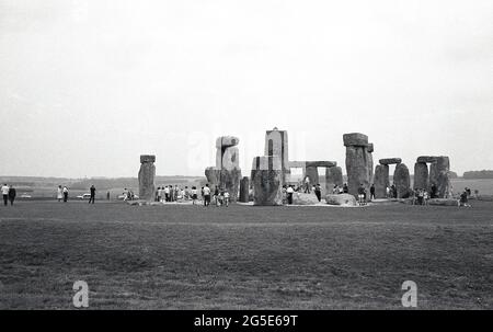 Anni '60, storico, vista esterna dei visitatori presso le antiche pietre di Stonehenge, Wiltshire, Inghilterra, Regno Unito. In questo periodo si poteva camminare liberamente intorno alle pietre preistoriche, ma nel decennio successivo a causa del numero di visitatori, danni all'erba e l'erosione al sacro, antico luogo di sepoltura, le pietre sono state rampate via impedendo l'accesso. Situato sulla Amesbury Abbey Estate, di proprietà di un tempo del re Enrico VIII, Cecil Chubb portò la terra con le pietre su un'asta nel 1915 e nel 1918 la diede alla nazione britannica. Foto Stock