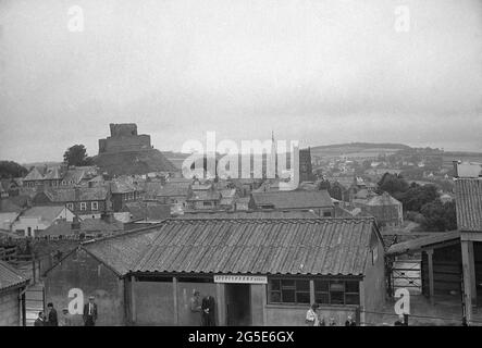 Anni '60, immagine storica che mostra una vista aerea sul mercato del bestiame di Launceston, Launceston, Cornovaglia, Inghilterra, Regno Unito con l'ufficio delle aste del mercato del bestiame in primo piano e l'antico mastio e la torre del castello di Launceston sullo sfondo. La guglia della chiesa della Maddalena di S. Maria è visibile sul retro a destra. Foto Stock