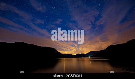 Una vista di un cielo notturno nuvoloso su Ullswater con Marte che oscilla attraverso le nuvole Foto Stock