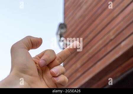 la mano fpv mostra il dito medio alla telecamera cctv nella strada pubblica della città Foto Stock