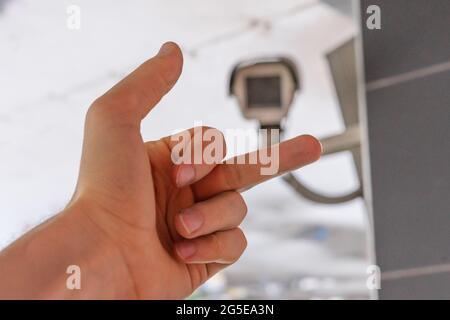 la mano fpv mostra il dito medio alla telecamera cctv nella strada pubblica della città Foto Stock