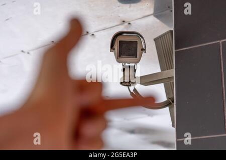 la mano fpv mostra il dito medio alla telecamera cctv nella strada pubblica della città Foto Stock