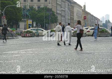 Due servitori d'altare hanno lasciato la chiesa e stanno attraversando l'Odeonsplatz Monaco, discutendo tra loro. Foto Stock