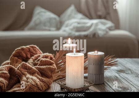 Accogliente composizione domestica con candele brucianti su un tavolo di legno con un elemento a maglia. Foto Stock