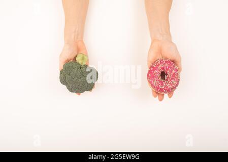 Confronto delle abitudini alimentari. Donna che tiene broccoli e ciambella su sfondo bianco Foto Stock