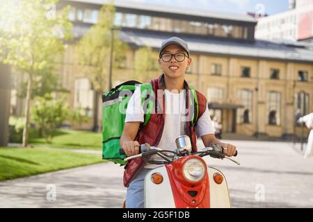 Giovane allegro corriero asiatico maschio con termo sacchetto sorridente a camma Foto Stock