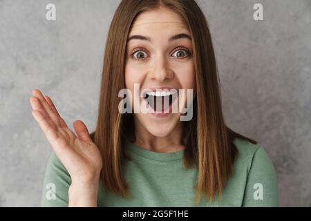 Eccitata bella ragazza piacevole che esprime sorpresa alla macchina fotografica isolata su parete grigia Foto Stock