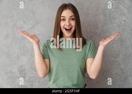 Eccitata bella ragazza che tiene e mostra copyspace isolato su parete grigia Foto Stock