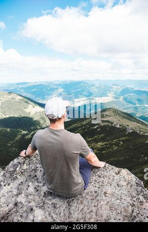 giovane uomo forte seduto sulla roccia in cima della cima della montagna Foto Stock