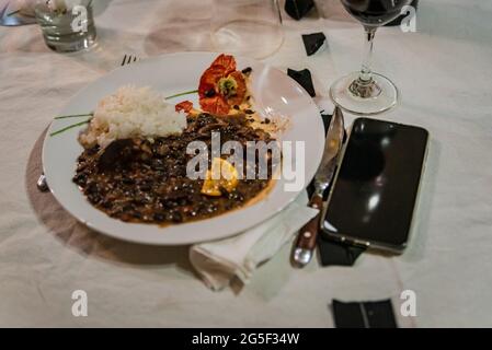 Piatto tipico brasiliano chiamato Feijoada. Prodotto con fagioli neri, maiale e salsiccia. Servito su un piatto bianco durante una riunione. Foto Stock