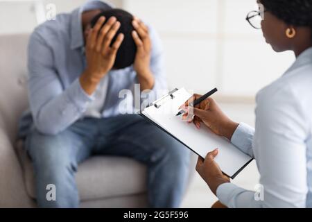 Concetto di psicoterapia. Ragazzo nero depresso che tiene la testa all'ufficio del consigliere, in cerca di aiuto professionale con il disordine mentale. Psico professionale Foto Stock